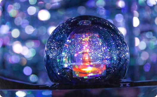 Een doorzichtige bol weerkaatst levendige, kleurrijke lichtjes, waardoor een caleidoscopisch effect ontstaat. De achtergrond is gevuld met zacht scherpgestelde bokeh-lichtjes, wat een dromerige sfeer oproept.