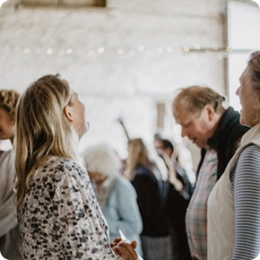 Een groep mensen in gesprek in een lichte, rustieke ruimte. De scène straalt een warme, gezellige sfeer uit, met zachte verlichting.